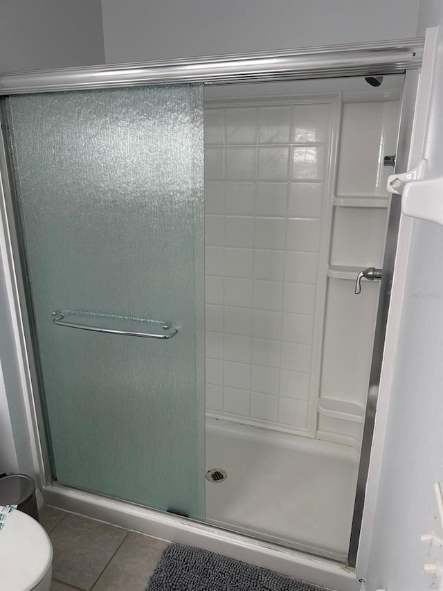 bathroom featuring toilet, a shower with door, and tile patterned floors