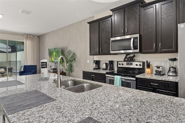 kitchen with dark brown cabinets, light stone countertops, stainless steel appliances, and sink