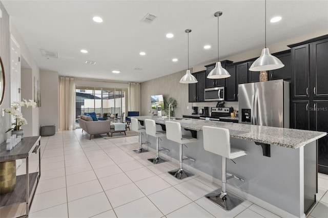 kitchen featuring a center island with sink, stainless steel appliances, hanging light fixtures, and a kitchen bar