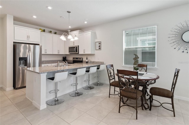 kitchen featuring light stone countertops, white cabinets, appliances with stainless steel finishes, and hanging light fixtures