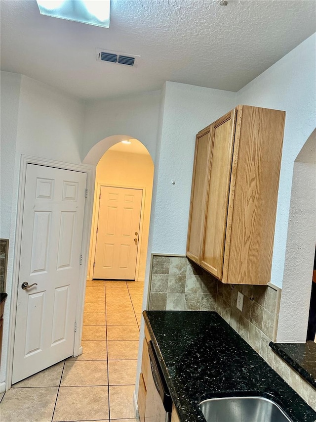 kitchen with sink, dark stone counters, a textured ceiling, decorative backsplash, and light tile patterned floors