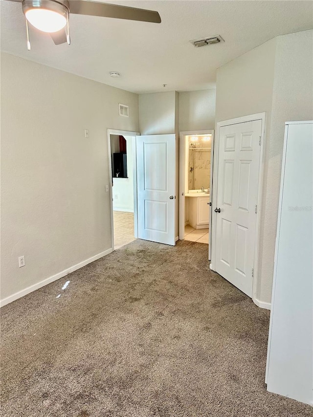 unfurnished bedroom with light colored carpet, ensuite bath, and ceiling fan