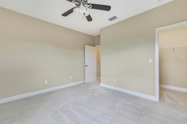 unfurnished bedroom with a walk in closet, a closet, ceiling fan, and light colored carpet