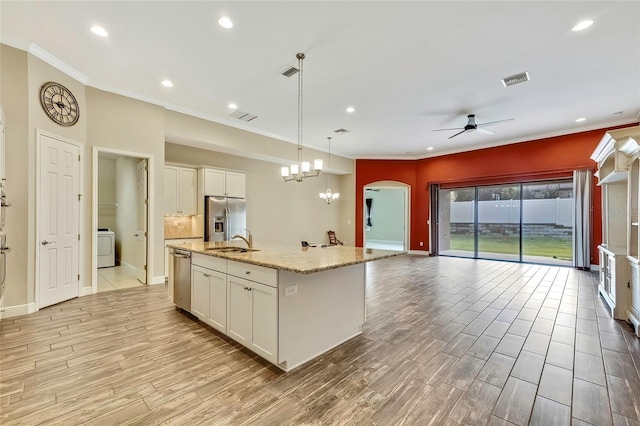 kitchen featuring light wood-type flooring, an island with sink, decorative light fixtures, white cabinetry, and stainless steel appliances