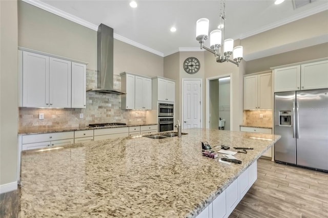 kitchen featuring sink, wall chimney range hood, light stone counters, white cabinets, and appliances with stainless steel finishes