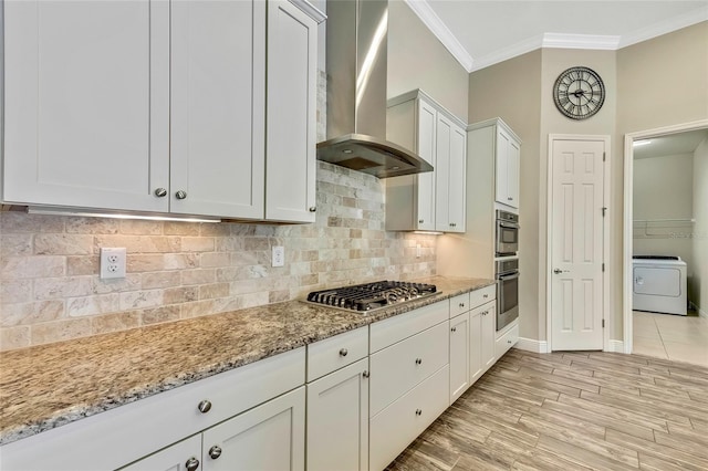 kitchen featuring white cabinets, wall chimney exhaust hood, light stone countertops, light hardwood / wood-style floors, and washer / dryer