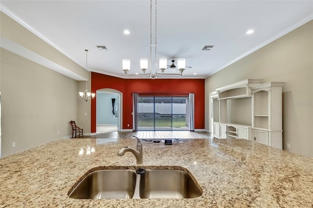 kitchen with light stone countertops, ornamental molding, sink, pendant lighting, and an inviting chandelier