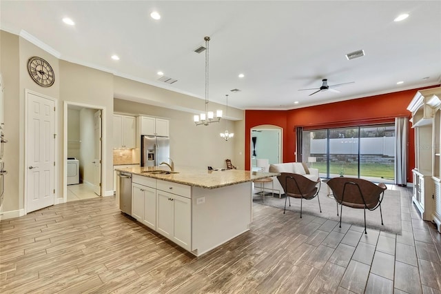 kitchen with ceiling fan with notable chandelier, stainless steel appliances, decorative light fixtures, light hardwood / wood-style flooring, and a center island with sink