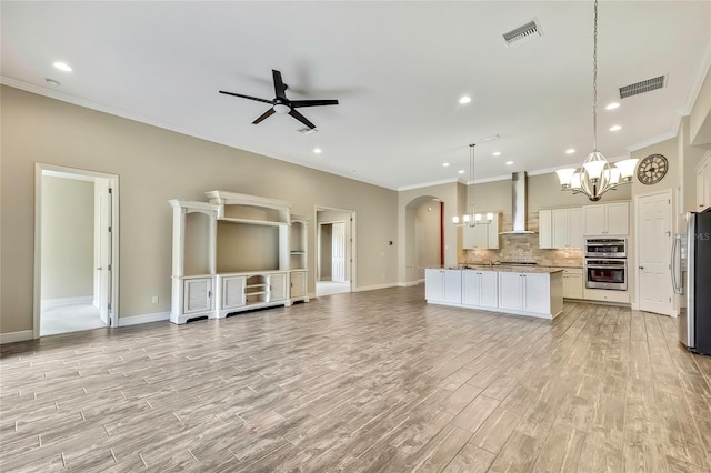 kitchen with stainless steel refrigerator, a center island, wall chimney exhaust hood, decorative light fixtures, and white cabinets