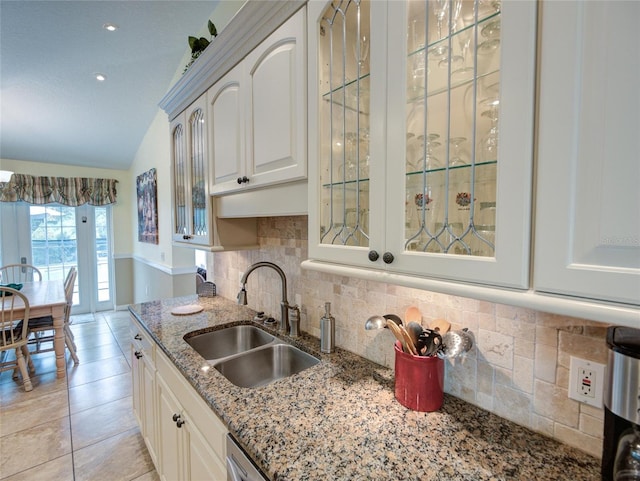 kitchen featuring decorative backsplash, white cabinets, light stone countertops, lofted ceiling, and sink