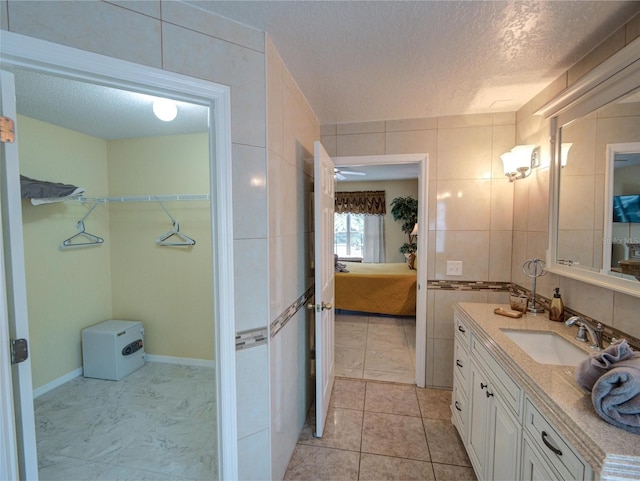 bathroom with a textured ceiling, tile walls, tile patterned flooring, and vanity