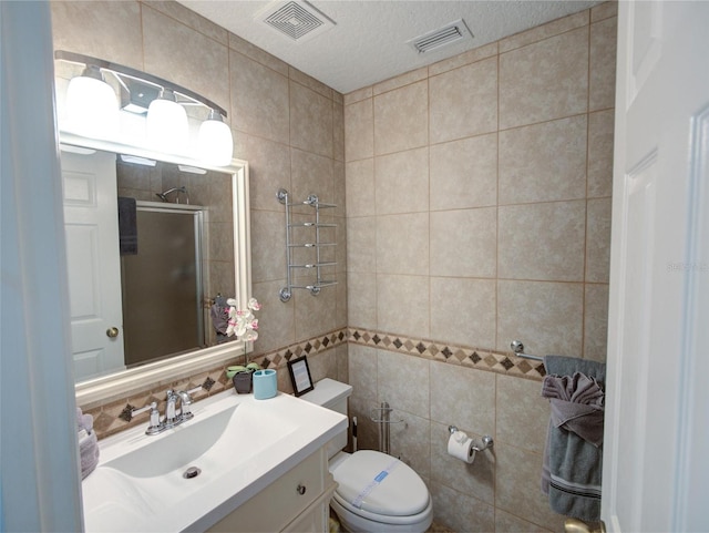 bathroom featuring tile walls, vanity, toilet, and a shower with shower door