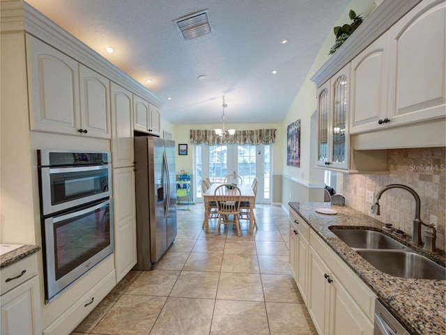 kitchen featuring sink, appliances with stainless steel finishes, a notable chandelier, light stone countertops, and vaulted ceiling