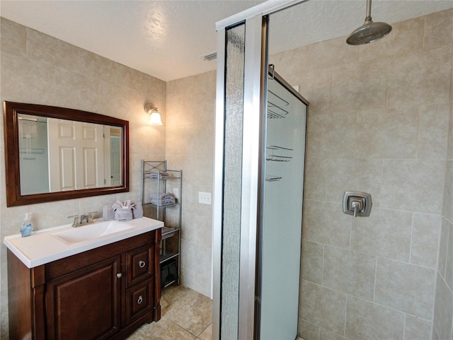 bathroom with tile walls, a textured ceiling, vanity, and tiled shower