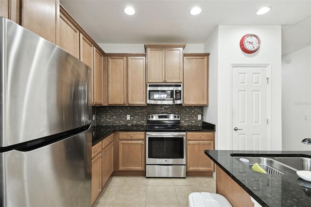 kitchen with light tile patterned flooring, sink, tasteful backsplash, stainless steel appliances, and dark stone countertops