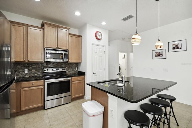 kitchen with sink, decorative light fixtures, a kitchen island with sink, stainless steel appliances, and dark stone counters