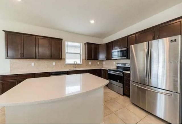 kitchen with light tile patterned floors, stainless steel appliances, a center island, dark brown cabinetry, and sink