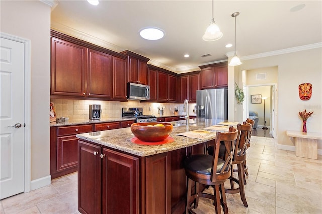 kitchen featuring an island with sink, decorative light fixtures, appliances with stainless steel finishes, and light stone countertops