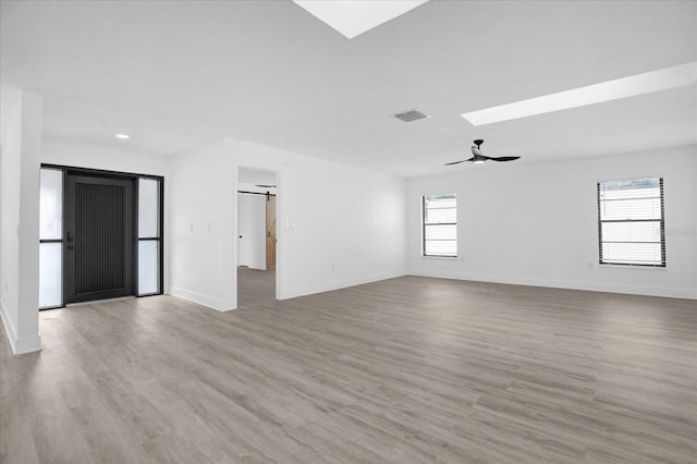 unfurnished living room with ceiling fan, a skylight, light hardwood / wood-style floors, and a wealth of natural light