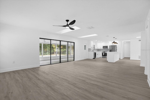 unfurnished living room featuring hardwood / wood-style floors, ceiling fan, a skylight, and sink