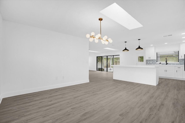 unfurnished living room featuring an inviting chandelier, a skylight, and hardwood / wood-style flooring