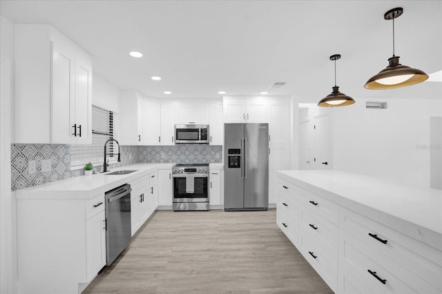 kitchen featuring white cabinets, stainless steel appliances, light wood-type flooring, decorative light fixtures, and sink