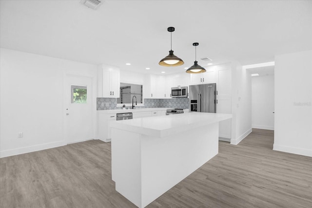 kitchen with white cabinets, a kitchen island, pendant lighting, stainless steel appliances, and light hardwood / wood-style flooring