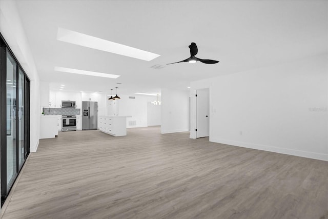 unfurnished living room featuring light hardwood / wood-style floors, ceiling fan, and a skylight