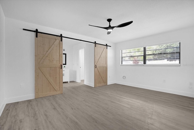 unfurnished bedroom featuring a barn door, wood-type flooring, and ceiling fan