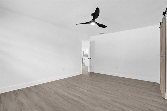 unfurnished room with ceiling fan, hardwood / wood-style flooring, and a barn door