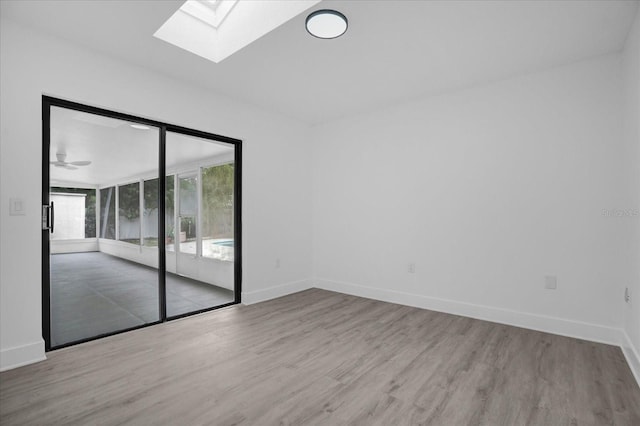 unfurnished room with ceiling fan, a skylight, and light hardwood / wood-style flooring