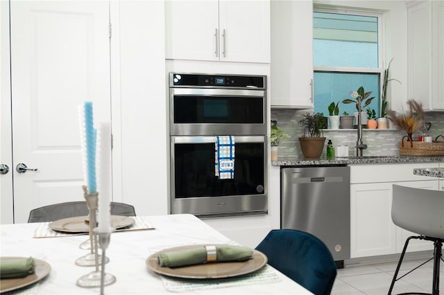 kitchen featuring appliances with stainless steel finishes, decorative backsplash, light stone counters, and white cabinets