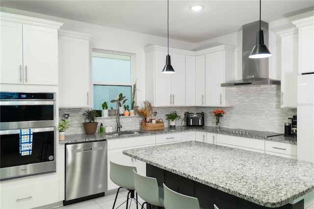 kitchen featuring pendant lighting, appliances with stainless steel finishes, wall chimney exhaust hood, and white cabinetry