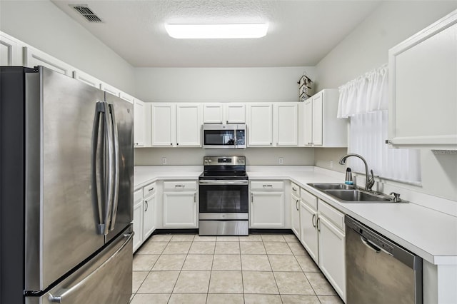 kitchen with sink, a textured ceiling, white cabinetry, stainless steel appliances, and light tile patterned floors