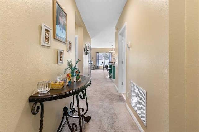 corridor featuring an inviting chandelier and light carpet