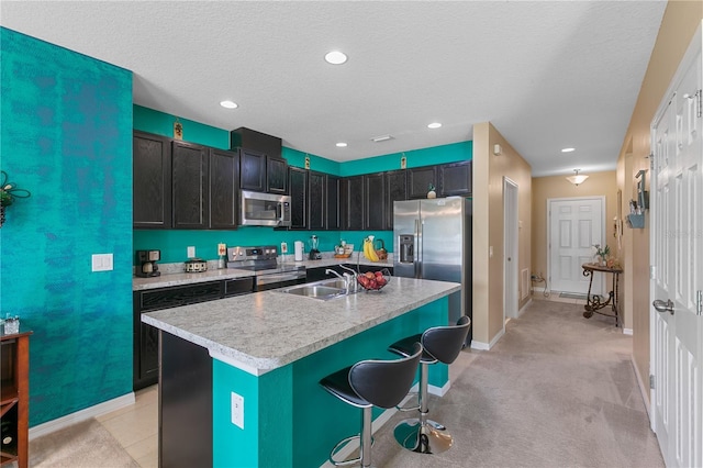 kitchen with sink, a kitchen island with sink, stainless steel appliances, a kitchen breakfast bar, and light colored carpet