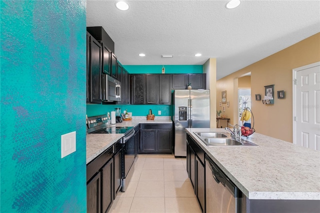 kitchen with light tile patterned floors, stainless steel appliances, a textured ceiling, a kitchen island with sink, and sink