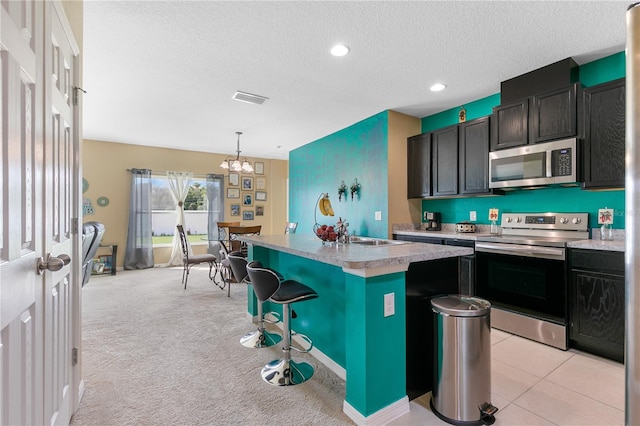 kitchen with a textured ceiling, a center island with sink, appliances with stainless steel finishes, a breakfast bar, and light colored carpet