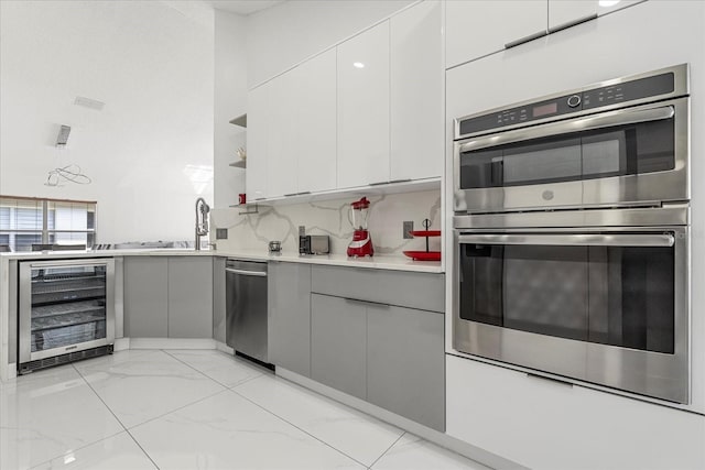 kitchen with appliances with stainless steel finishes, decorative backsplash, gray cabinetry, wine cooler, and white cabinets