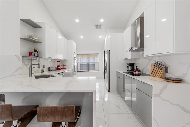 kitchen featuring white cabinetry, light stone counters, stainless steel refrigerator, kitchen peninsula, and wall chimney exhaust hood