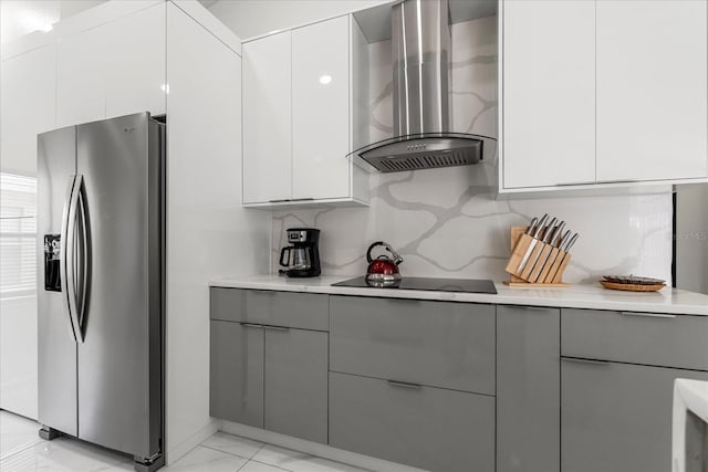 kitchen featuring gray cabinets, stainless steel refrigerator with ice dispenser, wall chimney range hood, and black electric cooktop