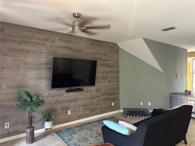 living room with wooden walls, ceiling fan, light tile patterned floors, and a textured ceiling