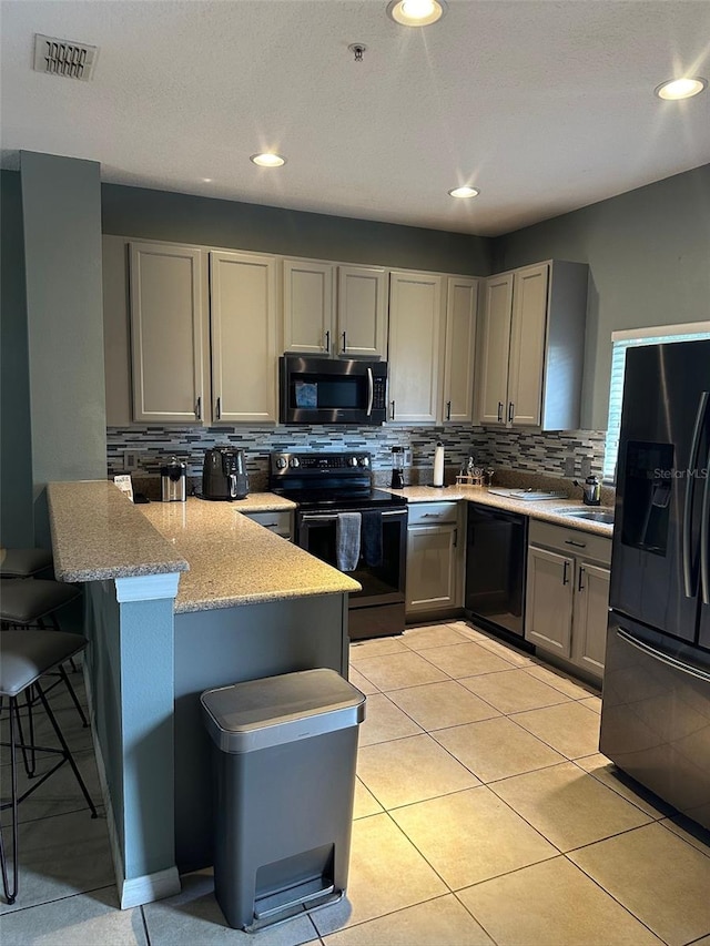 kitchen with a breakfast bar, gray cabinets, kitchen peninsula, decorative backsplash, and black appliances