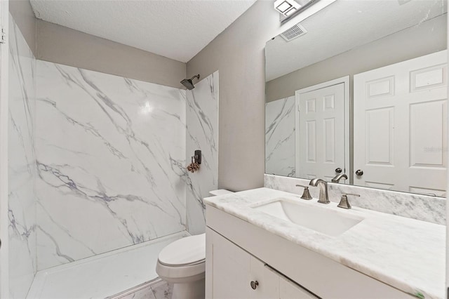 bathroom featuring vanity, a textured ceiling, a tile shower, and toilet