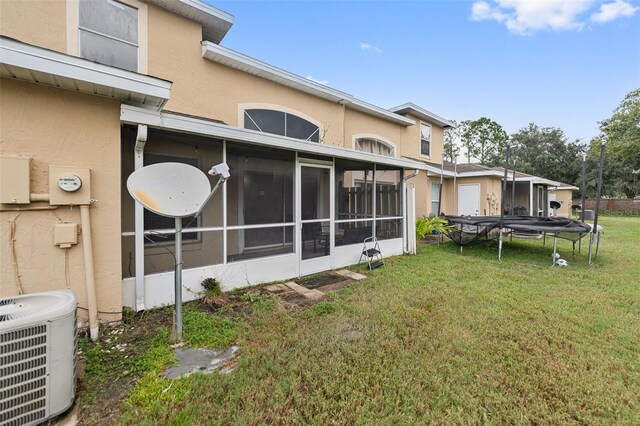 rear view of house with a sunroom, a trampoline, central AC, and a lawn