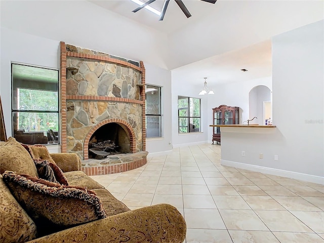 tiled living room featuring ceiling fan with notable chandelier and a stone fireplace