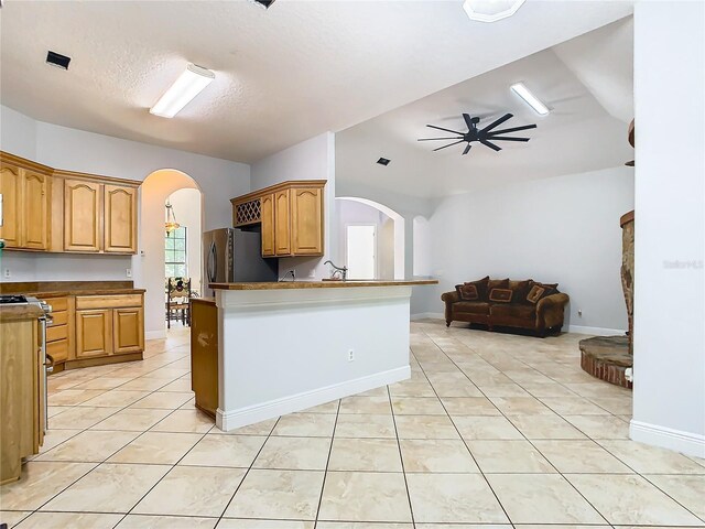 kitchen featuring kitchen peninsula, ceiling fan, light tile patterned flooring, and stainless steel fridge