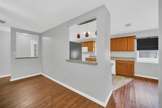 kitchen featuring light wood-type flooring, hanging light fixtures, white appliances, and kitchen peninsula