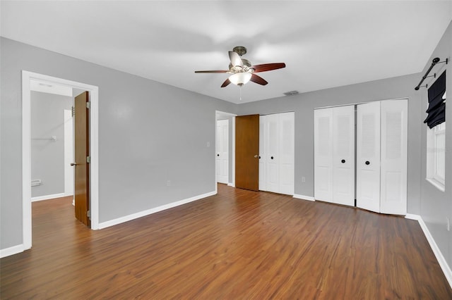 unfurnished bedroom with multiple closets, ceiling fan, and dark hardwood / wood-style flooring