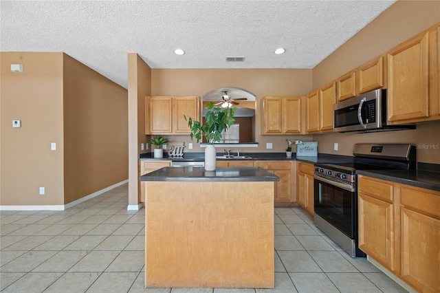 kitchen featuring light tile patterned flooring, stainless steel appliances, a textured ceiling, a center island, and ceiling fan